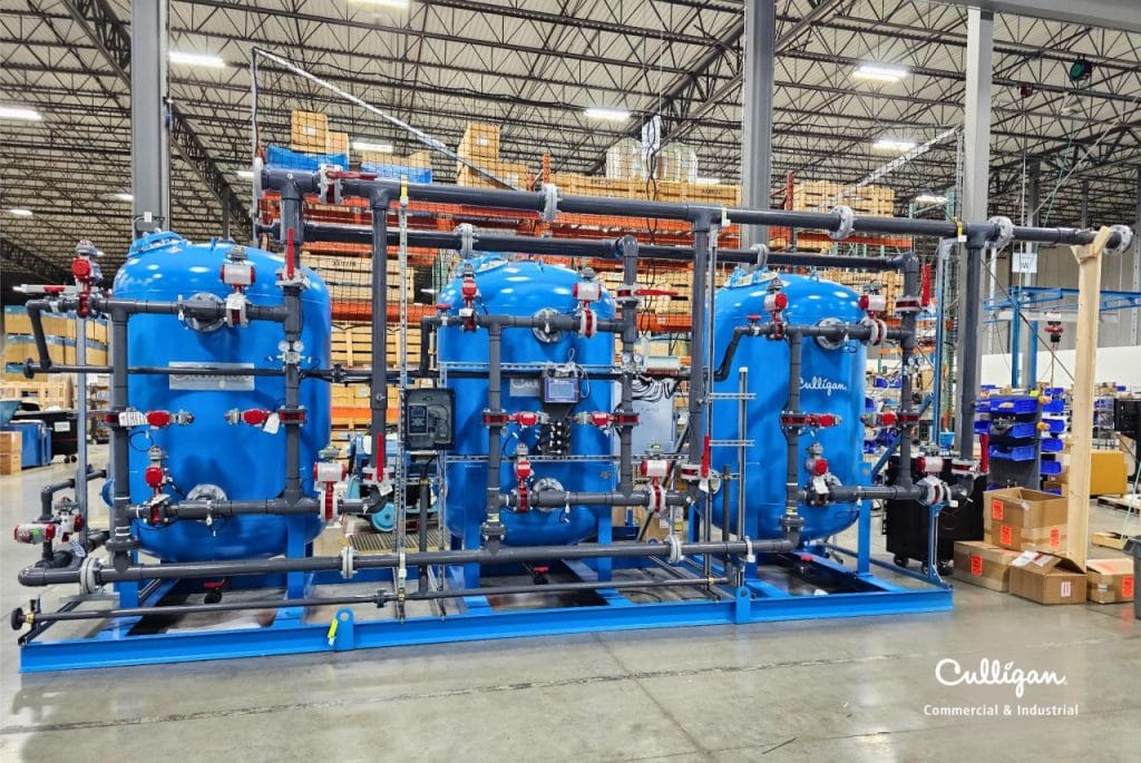 Système industriel de traitement de l'eau Culligan avec plusieurs réservoirs bleus et un réseau complexe de tuyauterie, installé dans un entrepôt.