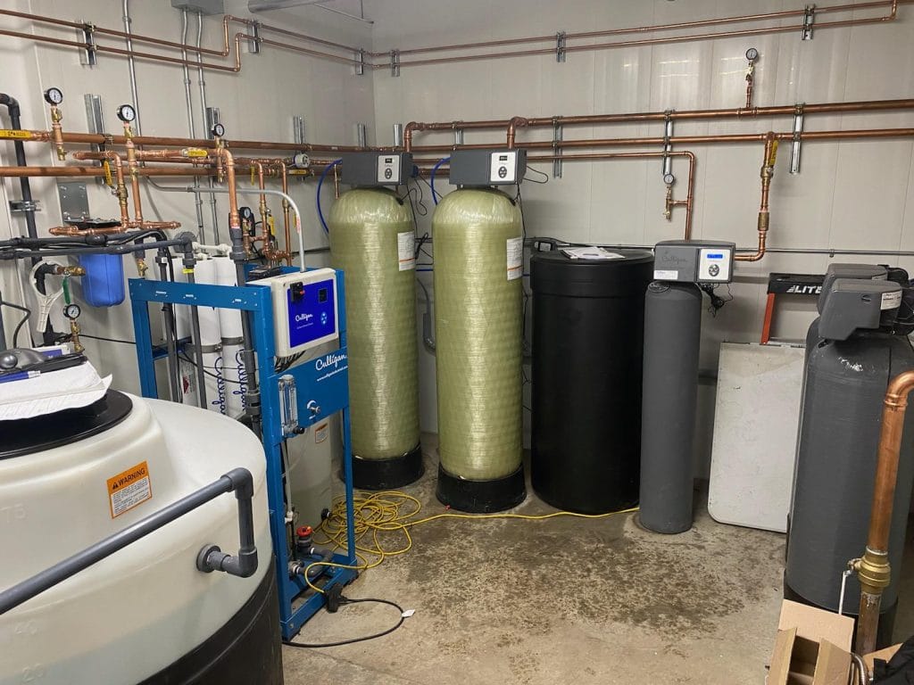 "Système complet de traitement de l'eau Culligan installé dans une salle technique, comprenant des réservoirs, des filtres, et des équipements de surveillance, avec des tuyaux en cuivre le long des murs."
