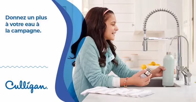 Petite fille souriante qui remplie une bouteille d'eau avec le robinet Culligan dans la cuisine